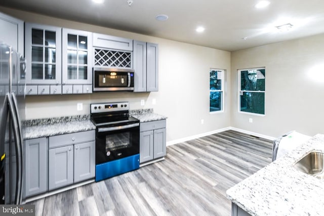 kitchen featuring light stone countertops, stainless steel appliances, gray cabinetry, and light hardwood / wood-style floors