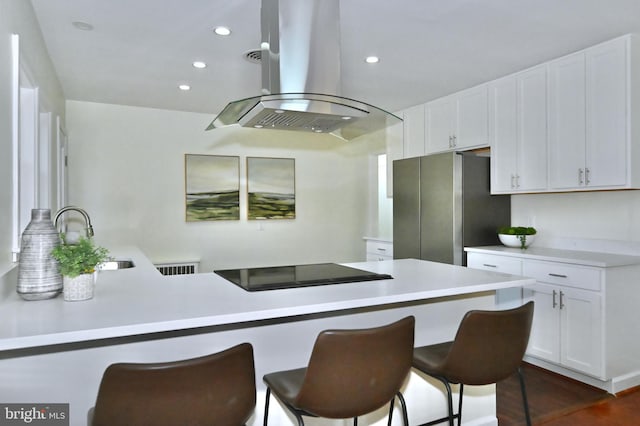 kitchen featuring black electric cooktop, white cabinetry, island range hood, and stainless steel refrigerator