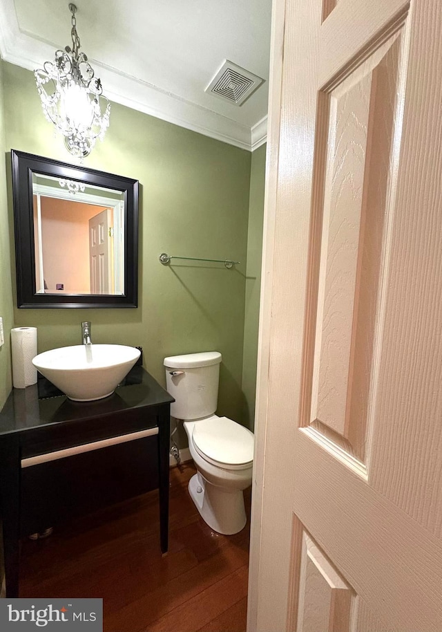 bathroom featuring wood-type flooring, a chandelier, vanity, toilet, and crown molding