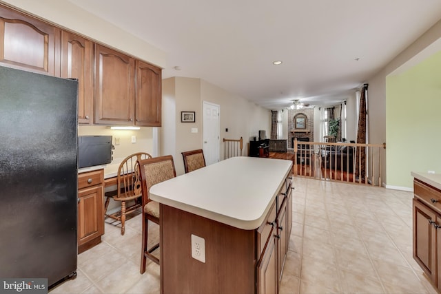 kitchen with ceiling fan, black refrigerator, a kitchen bar, a fireplace, and a kitchen island