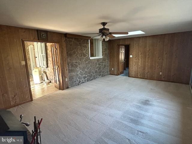 carpeted empty room featuring a skylight, wooden walls, and ceiling fan