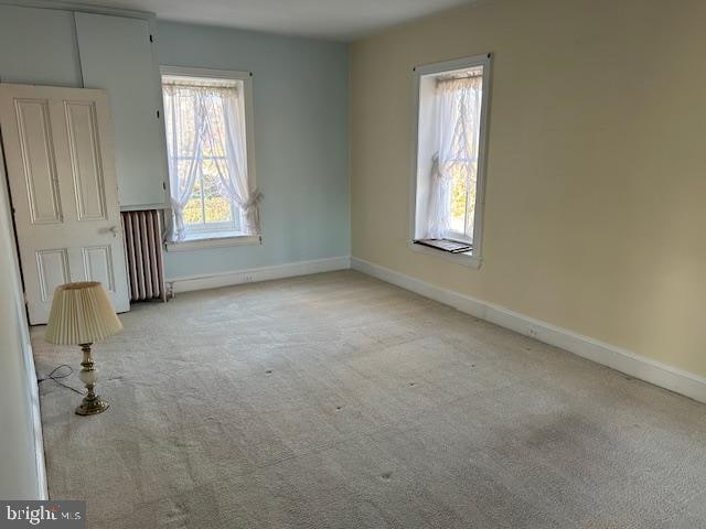 empty room with light colored carpet, a healthy amount of sunlight, and radiator heating unit