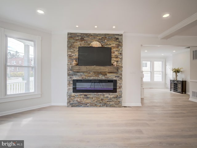 unfurnished living room with a healthy amount of sunlight, a stone fireplace, ornamental molding, and light hardwood / wood-style flooring