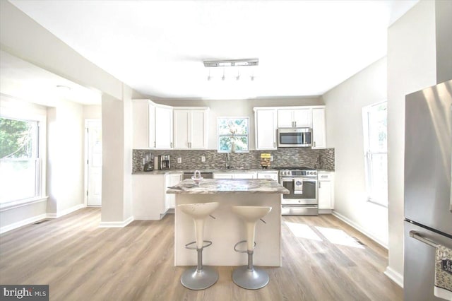 kitchen featuring appliances with stainless steel finishes, a center island, white cabinetry, and a healthy amount of sunlight