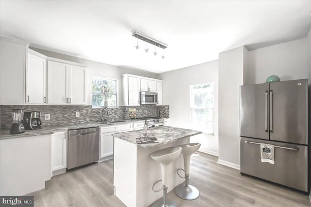 kitchen with sink, a kitchen island, appliances with stainless steel finishes, light hardwood / wood-style floors, and white cabinetry