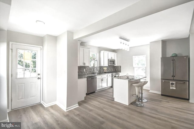 kitchen featuring appliances with stainless steel finishes, dark hardwood / wood-style flooring, a breakfast bar, a kitchen island, and white cabinetry