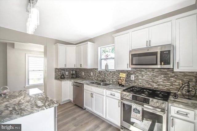 kitchen featuring appliances with stainless steel finishes, light wood-type flooring, tasteful backsplash, sink, and white cabinetry