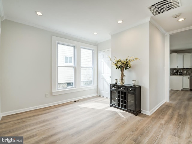 interior space featuring backsplash, light wood-type flooring, white cabinetry, and ornamental molding