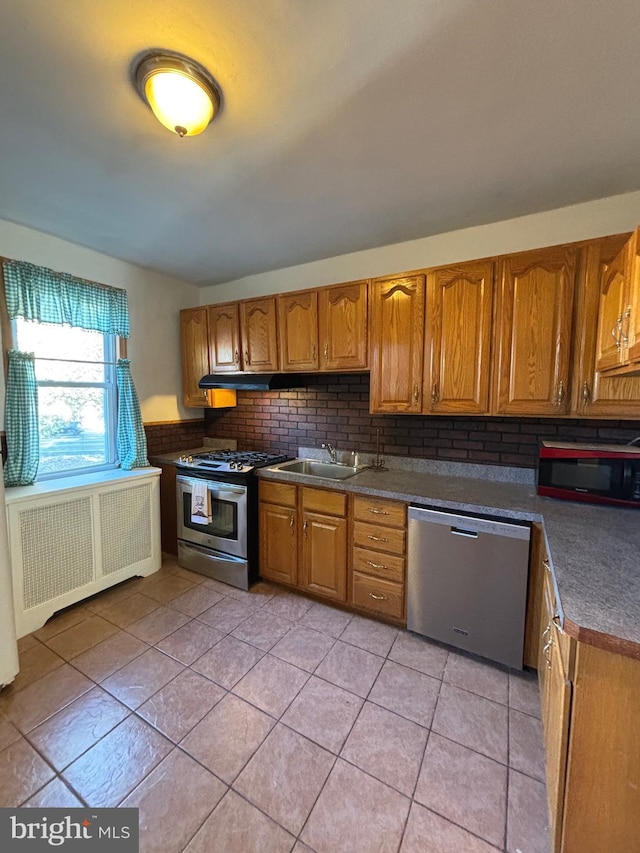 kitchen with tasteful backsplash, sink, radiator, stainless steel appliances, and light tile patterned floors