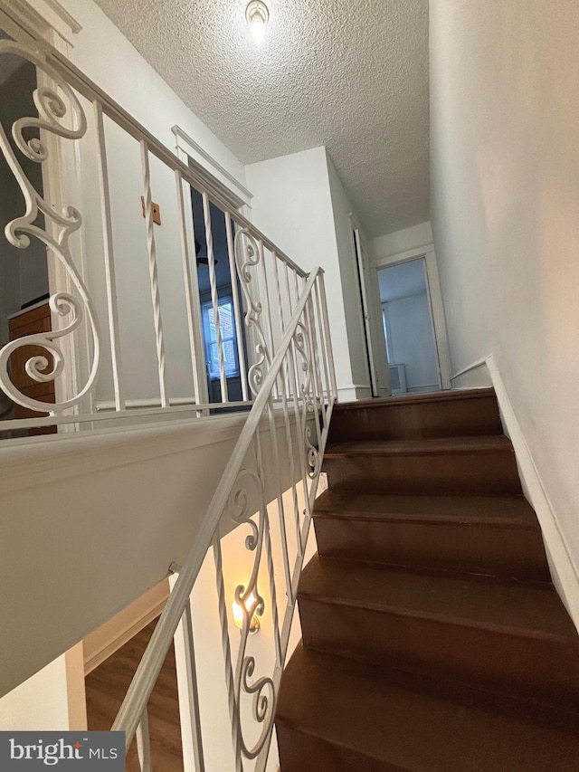 staircase featuring a textured ceiling and hardwood / wood-style flooring