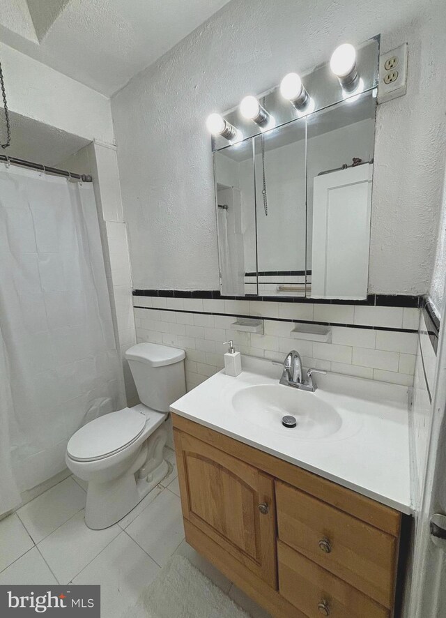 bathroom with walk in shower, tile walls, toilet, vanity, and tile patterned floors