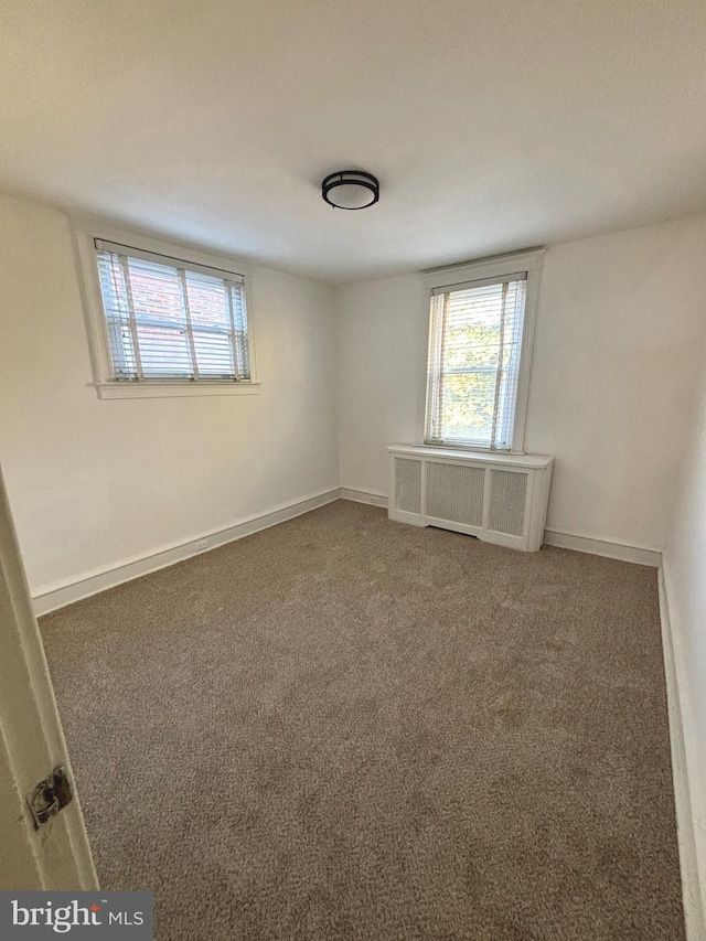 spare room featuring radiator and dark carpet