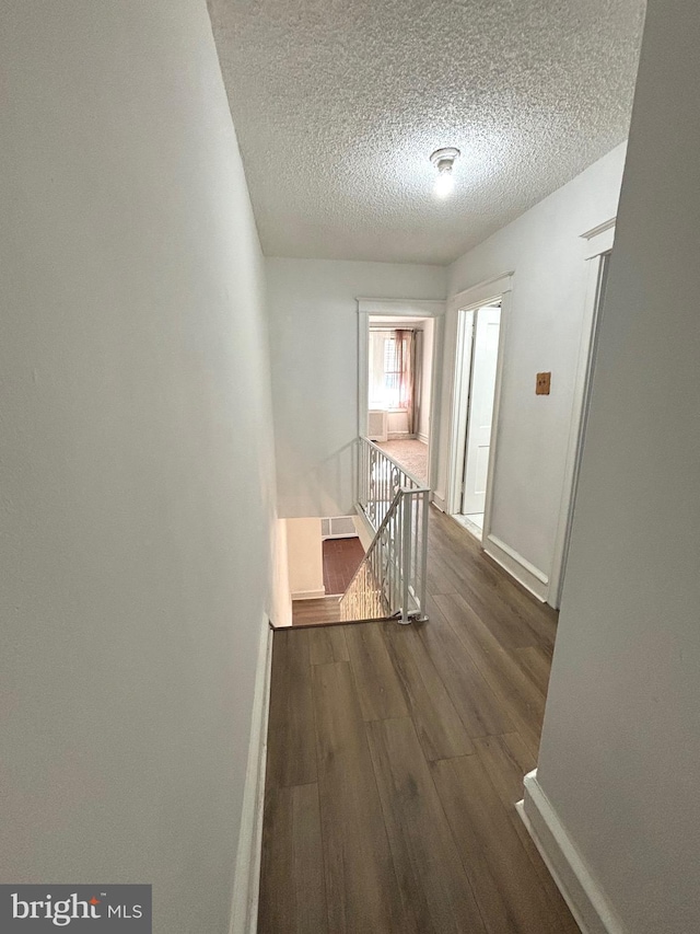 corridor with a textured ceiling and dark hardwood / wood-style flooring