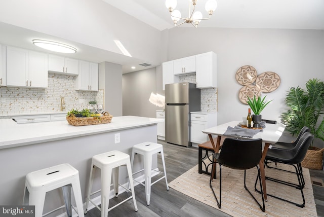 kitchen with a breakfast bar, decorative backsplash, stainless steel fridge, white cabinetry, and wood-type flooring