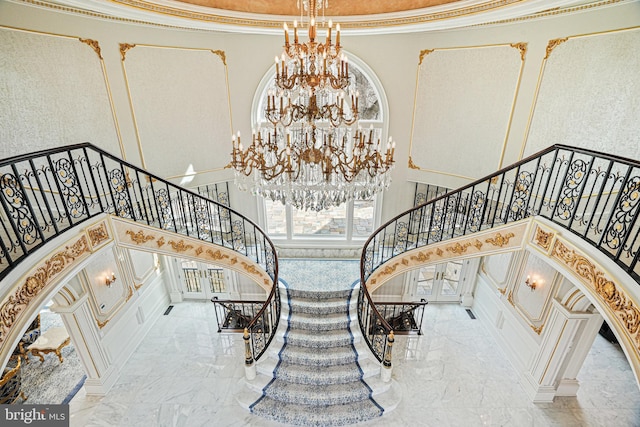 stairway featuring a towering ceiling, crown molding, and a chandelier