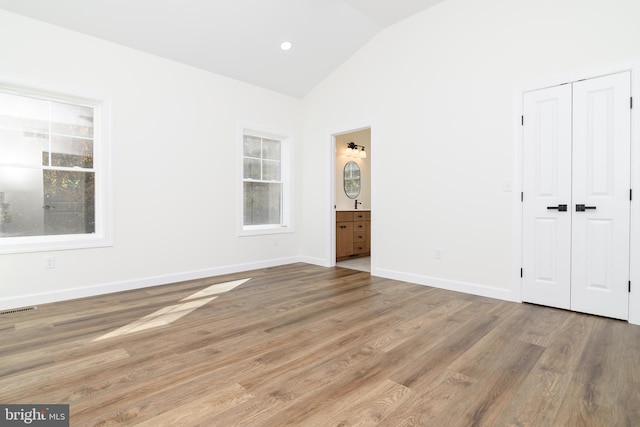 unfurnished bedroom featuring ensuite bath, wood-type flooring, and vaulted ceiling