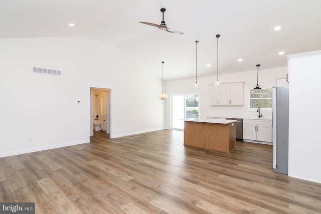 kitchen with appliances with stainless steel finishes, white cabinetry, light wood-type flooring, vaulted ceiling, and a center island