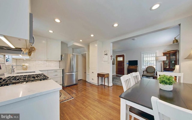 kitchen with sink, decorative backsplash, white cabinetry, stainless steel refrigerator, and light hardwood / wood-style flooring