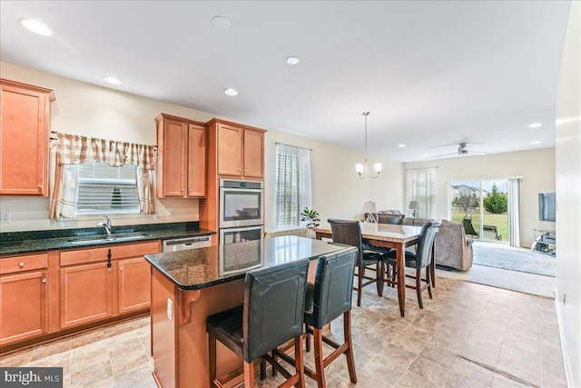 kitchen with ceiling fan with notable chandelier, sink, dark stone countertops, a kitchen island, and stainless steel appliances