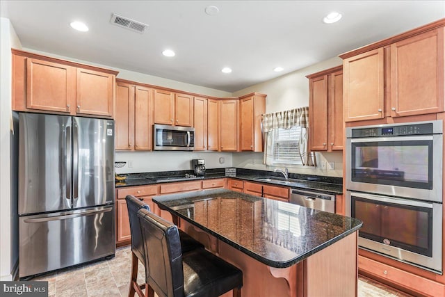 kitchen featuring a kitchen bar, appliances with stainless steel finishes, dark stone counters, sink, and a kitchen island