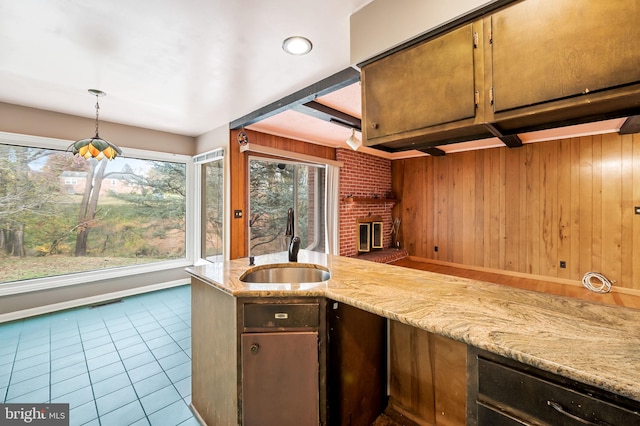 kitchen with wood walls, sink, light stone countertops, hanging light fixtures, and a brick fireplace