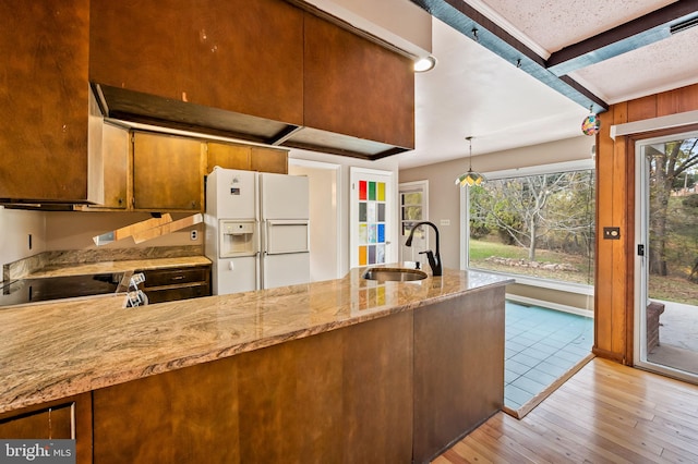 kitchen featuring sink, white fridge with ice dispenser, light stone countertops, pendant lighting, and light wood-type flooring