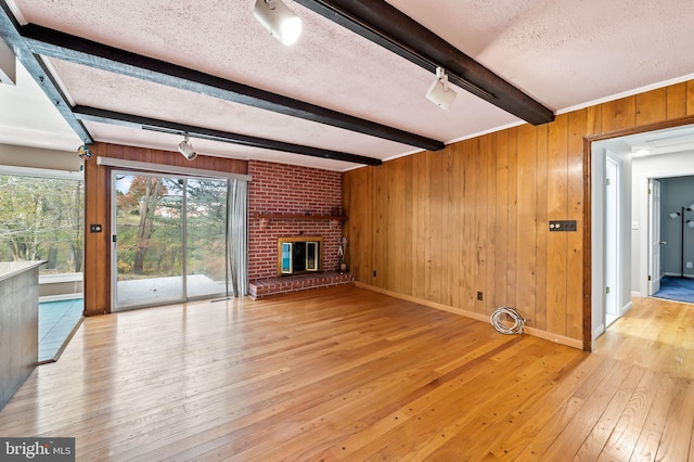 unfurnished living room with a fireplace, light hardwood / wood-style flooring, a textured ceiling, and beam ceiling