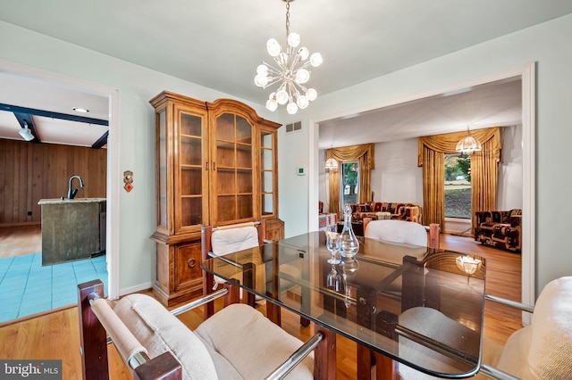 dining area featuring beamed ceiling, wood-type flooring, a chandelier, and wooden walls