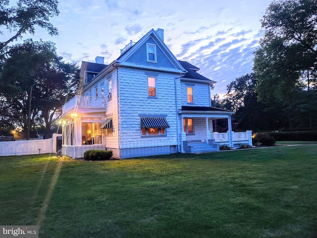 back house at dusk featuring covered porch and a lawn