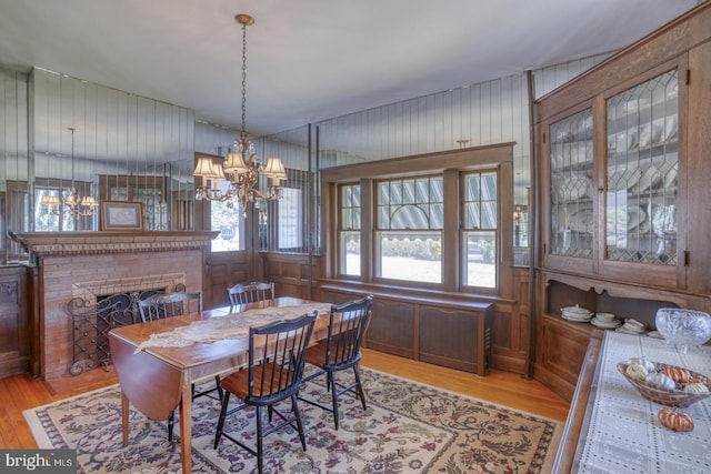 dining room featuring wood walls, light wood-type flooring, an inviting chandelier, and a fireplace