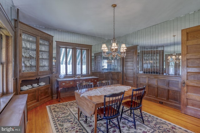 dining area featuring light wood-type flooring, wood walls, and a chandelier