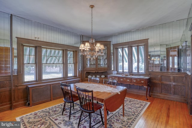 dining room with light hardwood / wood-style floors, a wealth of natural light, wooden walls, and a chandelier