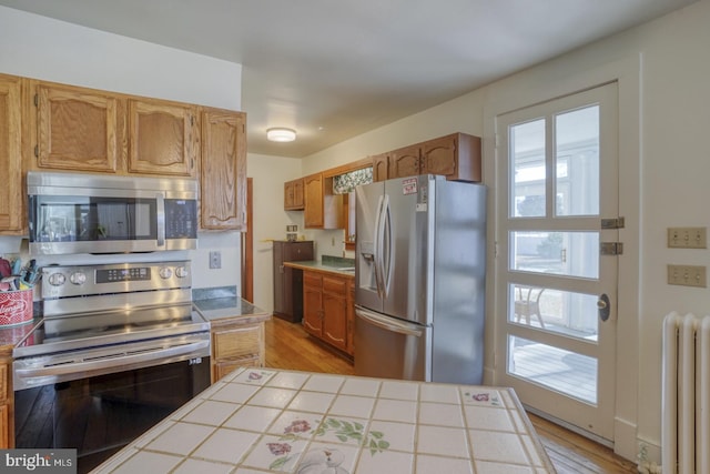 kitchen featuring tile countertops, radiator, light hardwood / wood-style flooring, and stainless steel appliances