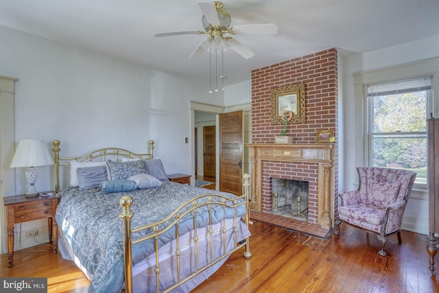 bedroom featuring a brick fireplace, hardwood / wood-style floors, and ceiling fan