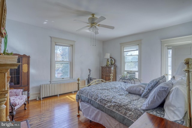 bedroom featuring ceiling fan, multiple windows, radiator heating unit, and light wood-type flooring