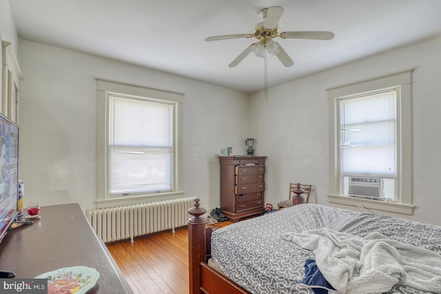 bedroom featuring wood-type flooring, multiple windows, ceiling fan, and radiator