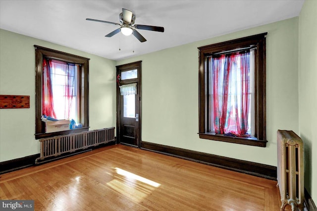 unfurnished room with hardwood / wood-style floors, radiator, and ceiling fan