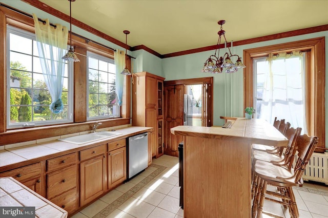 kitchen with stainless steel dishwasher, hanging light fixtures, tile counters, and a healthy amount of sunlight