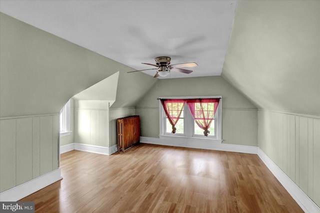 additional living space with light hardwood / wood-style floors, lofted ceiling, radiator heating unit, and ceiling fan