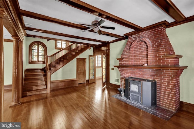 unfurnished living room with ornate columns, beam ceiling, a wood stove, and dark hardwood / wood-style flooring