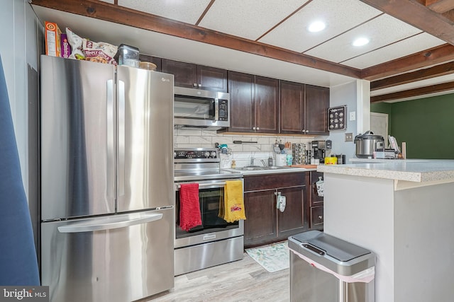 kitchen with dark brown cabinets, tasteful backsplash, appliances with stainless steel finishes, and light hardwood / wood-style flooring