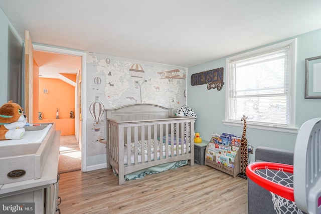 bedroom with light hardwood / wood-style floors and a nursery area