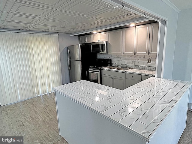 kitchen with tile countertops, gray cabinets, light wood-type flooring, and appliances with stainless steel finishes