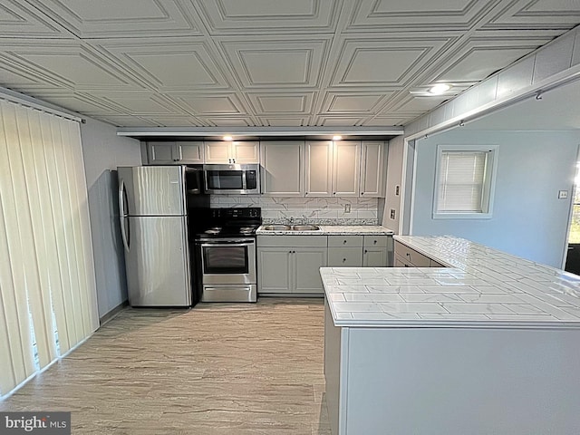 kitchen featuring gray cabinetry, sink, light hardwood / wood-style floors, kitchen peninsula, and stainless steel appliances