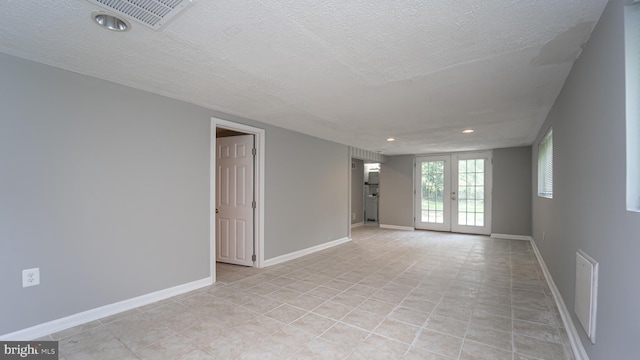 tiled empty room with french doors and a textured ceiling