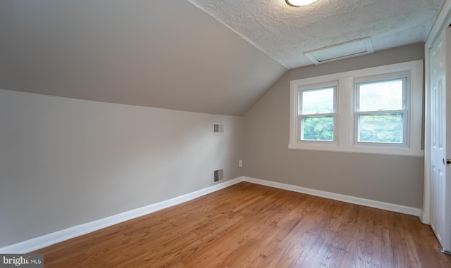 bonus room with light hardwood / wood-style floors, lofted ceiling, and a textured ceiling