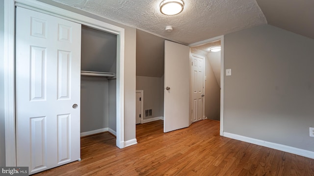 unfurnished bedroom featuring a closet, a textured ceiling, lofted ceiling, and light wood-type flooring