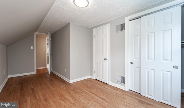 additional living space featuring light hardwood / wood-style floors, lofted ceiling, and a textured ceiling