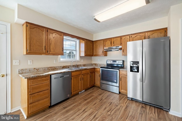 kitchen featuring a textured ceiling, light wood-type flooring, appliances with stainless steel finishes, and sink