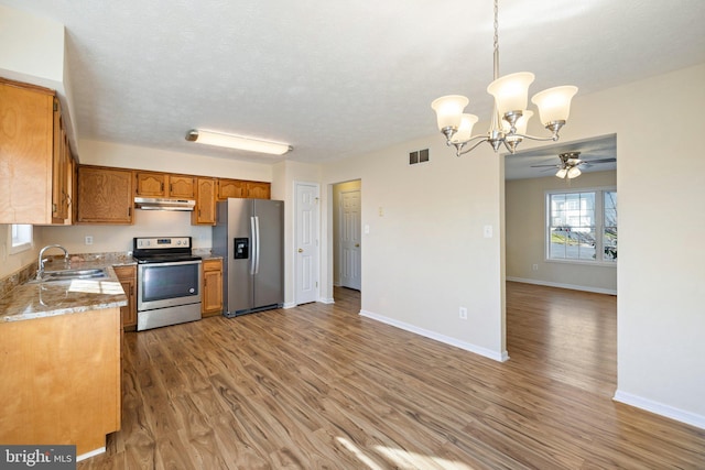 kitchen with stainless steel appliances, hardwood / wood-style flooring, sink, ceiling fan with notable chandelier, and decorative light fixtures